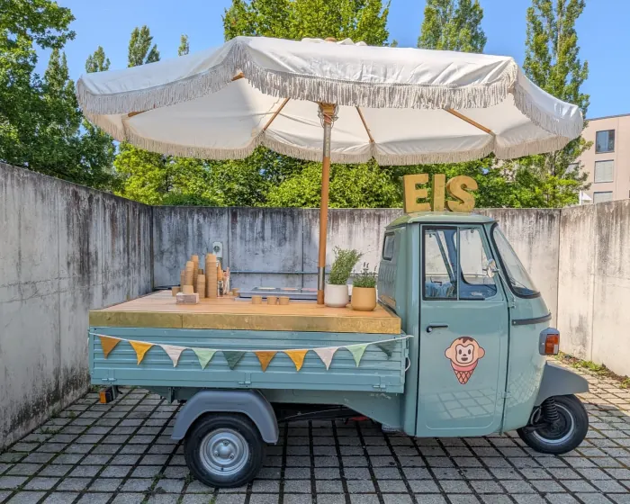 Die Eis-Ape mit Sonnenschirm, Wimpelkette und EIS-Schriftzug in einem Innenhof
