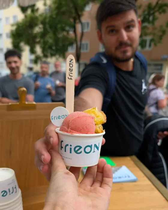 Ein Becher Bio-Eis mit gebrandetem Holzlöffel wird über den Tisch gereicht