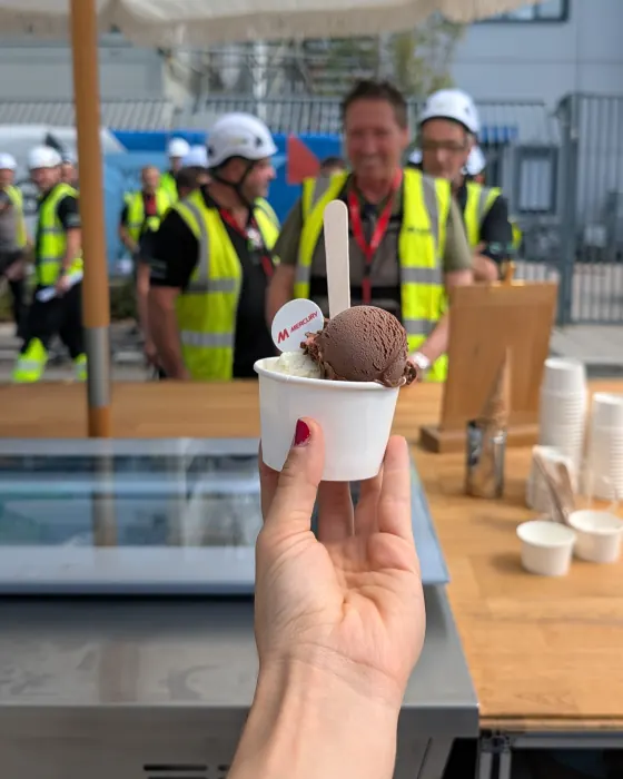 Eisbecher mit essbarem Mercury-Logo, dahinter Gäste in Warnwesten