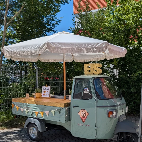 Die Eis-Ape mit Sonnenschirm, EIS-Schriftzug und Wimpelkette im Schatten